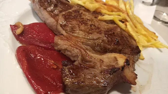 Un plato blanco cubierto con un filete, pimientos y patatas fritas.