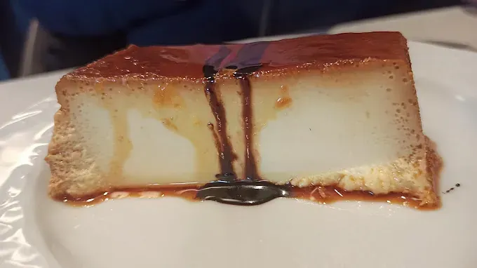Una rebanada de flan con salsa de chocolate en un plato blanco.