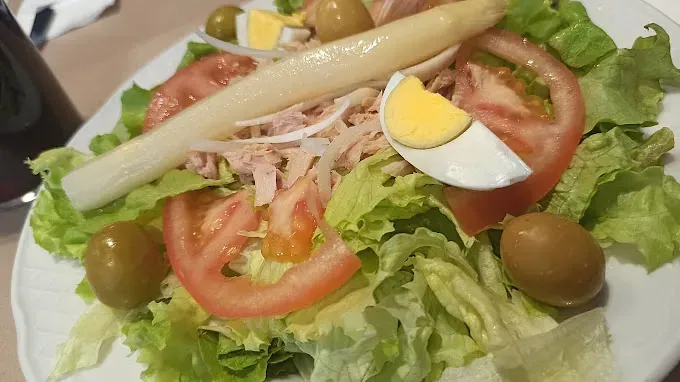Una ensalada con lechuga, tomates, huevos, aceitunas y espárragos en un plato blanco.