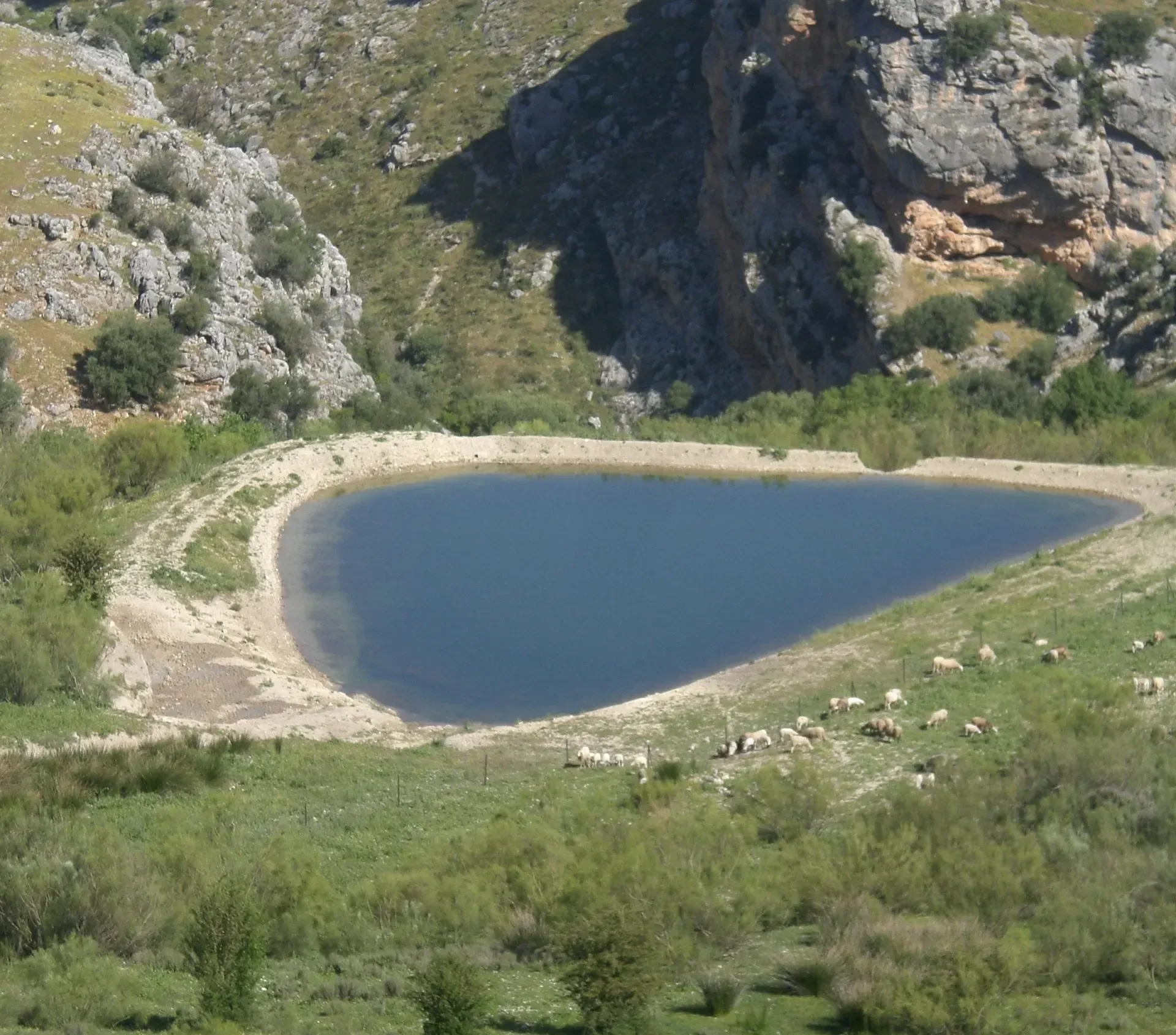 Un tranquilo lago azul ubicado en un valle rodeado de acantilados rocosos y vegetación verde.
