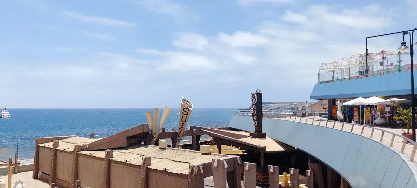 Vista frente al mar de un edificio con techo azul, bar de playa y cielo azul.