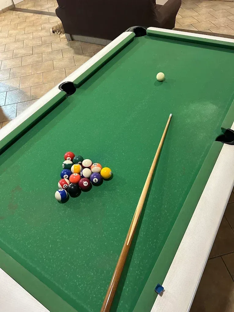 Mesa de billar con bolas colocadas, taco de billar y bola blanca sobre una superficie de fieltro verde.