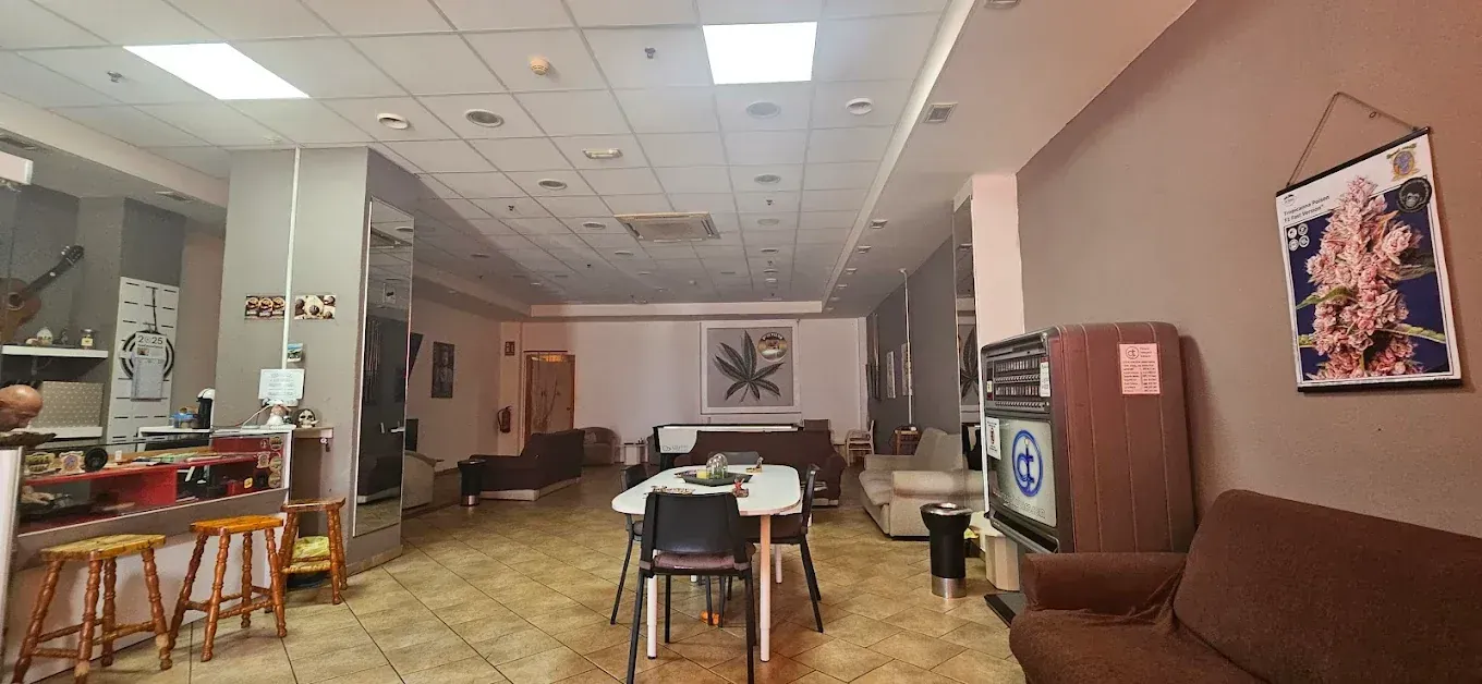 Una sala con mesas, sillas y sofás. Hay un póster colgado en la pared y un televisor.