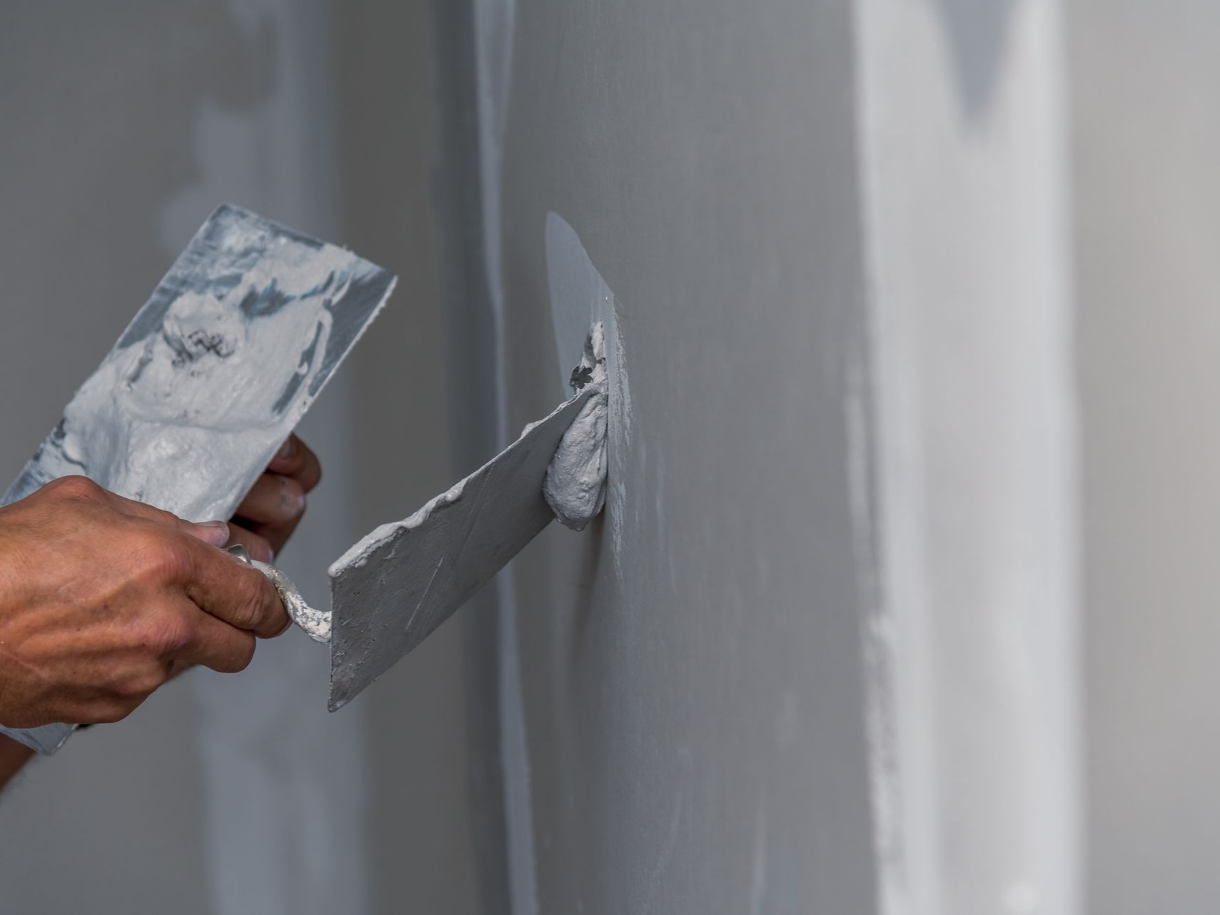 Une personne utilise une truelle pour appliquer du mastic sur un mur, en lissant la surface.
