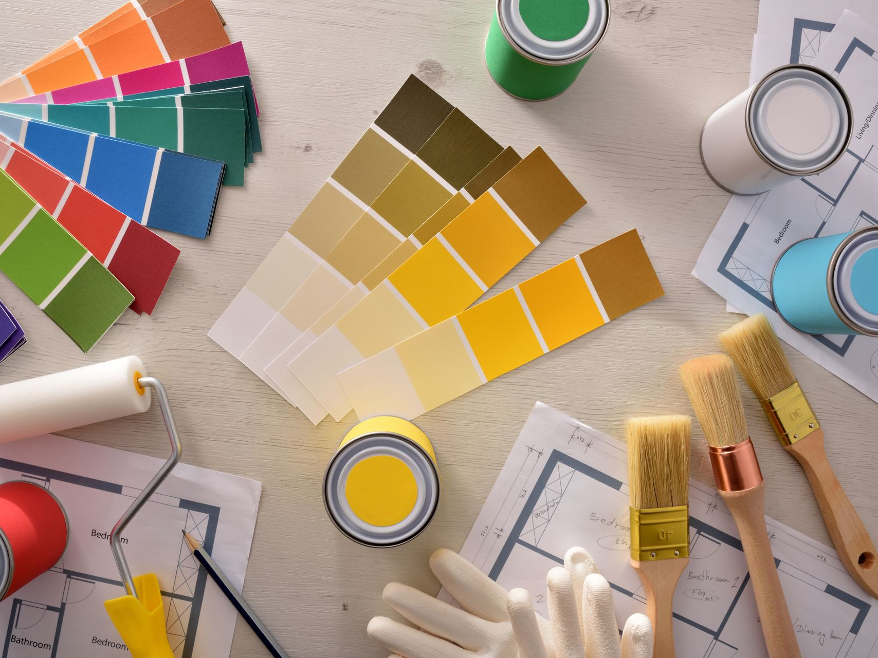 Échantillons de peinture, pots, pinceaux, rouleau, gants et plans sur une surface en bois, mettant en évidence le choix des couleurs.