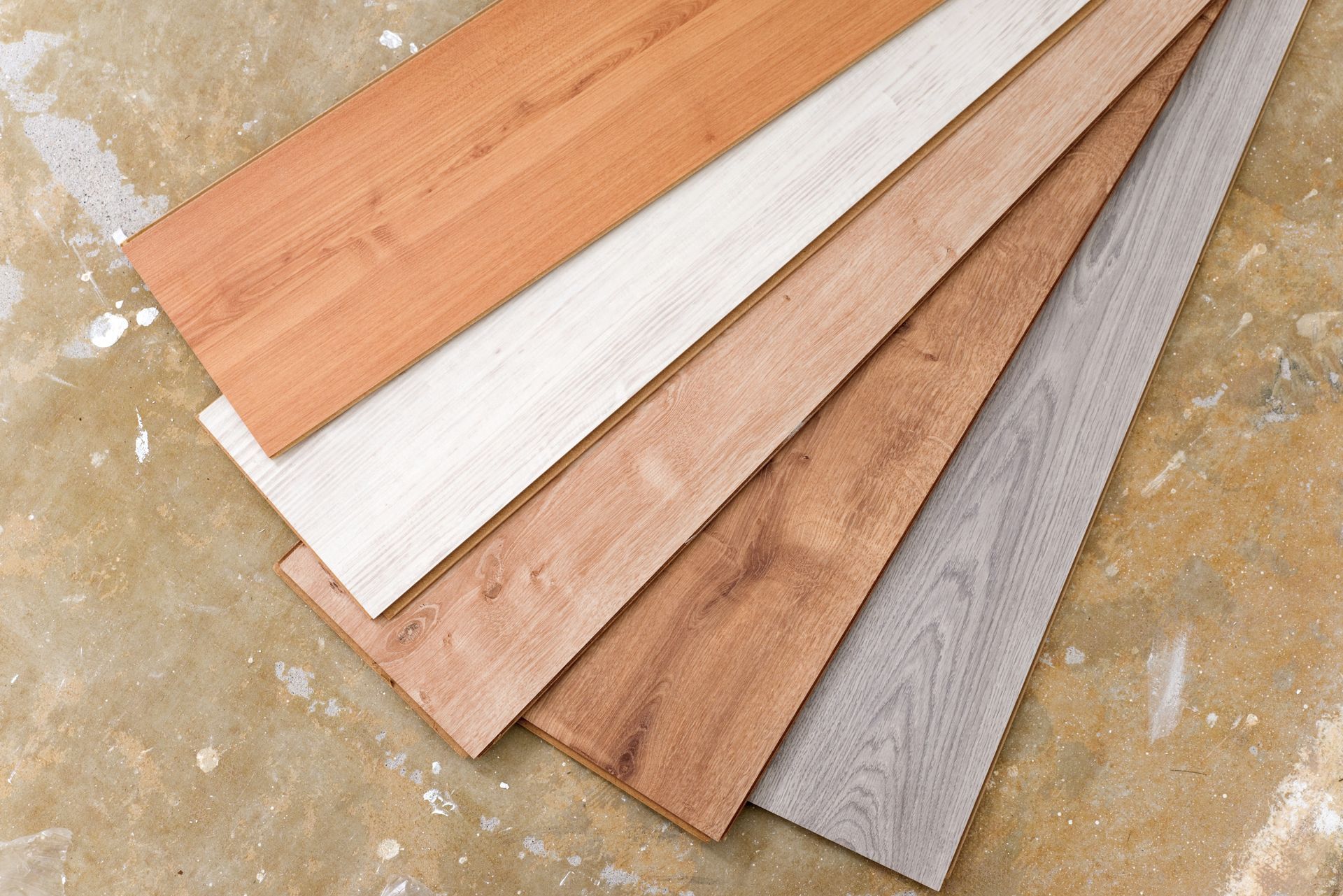 Cinq échantillons de parquet en bois de différentes teintes sur une surface texturée brun clair.