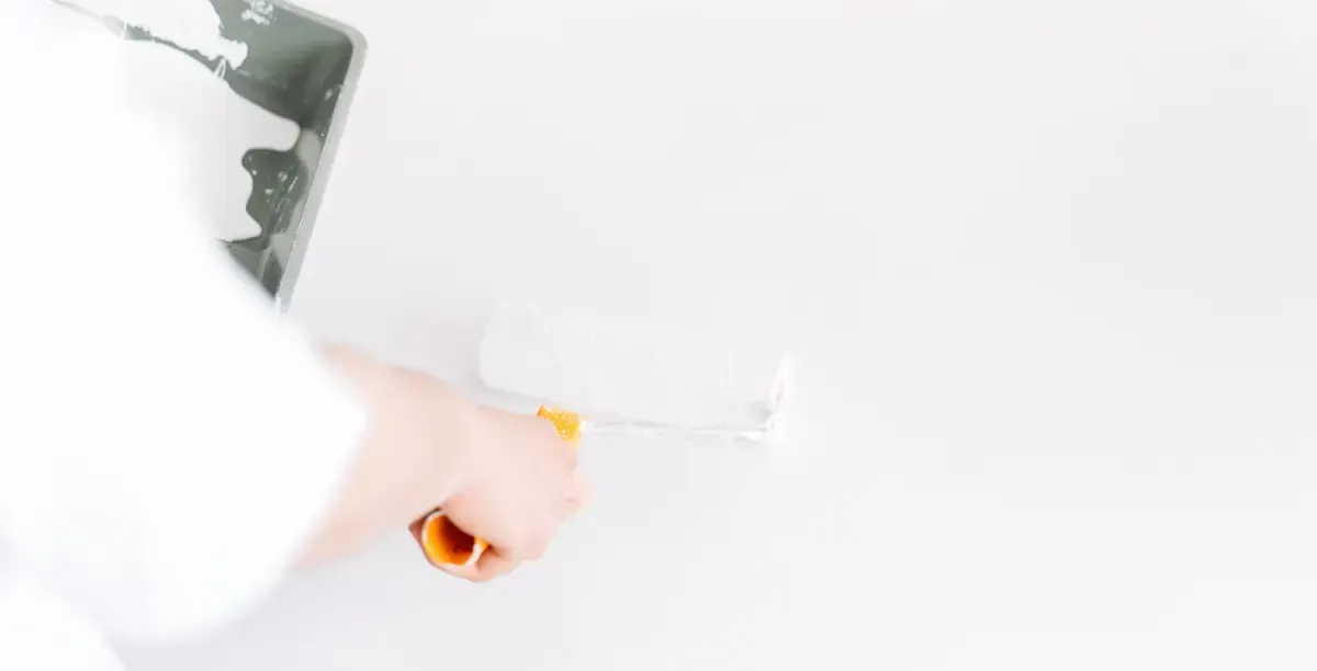 Persona pintando una pared blanca con un rodillo de pintura.