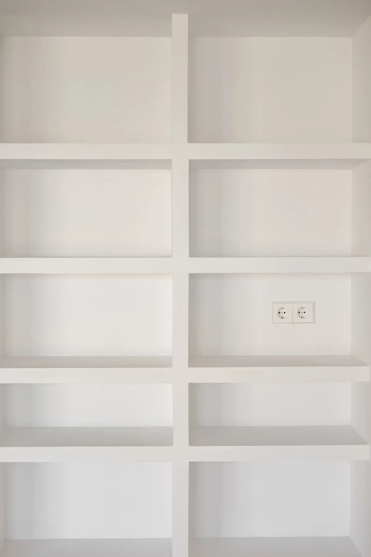 Estantería empotrada blanca vacía con varios compartimentos. Incluye toma de corriente en una sección.