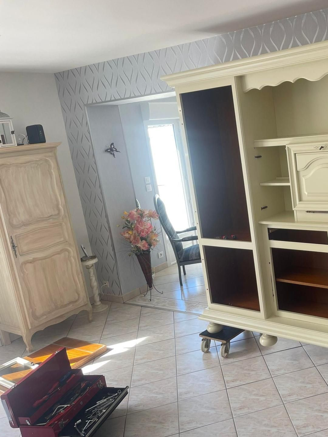 Une armoire couleur crème et un meuble TV dans un salon avec une caisse à outils posée sur le sol.