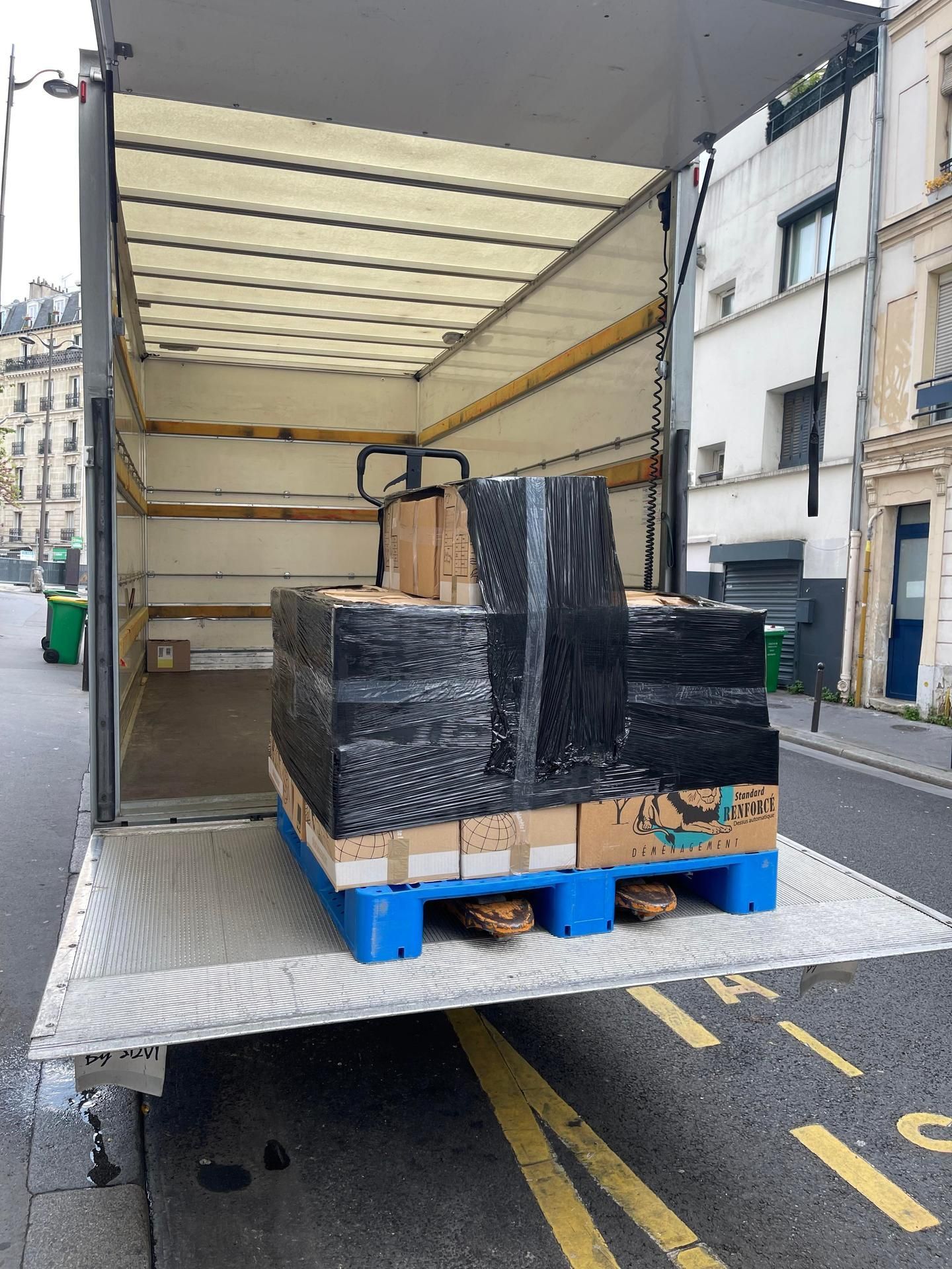 Des cartons, des balais, des outils et un transpalette à l'extérieur d'un bâtiment.