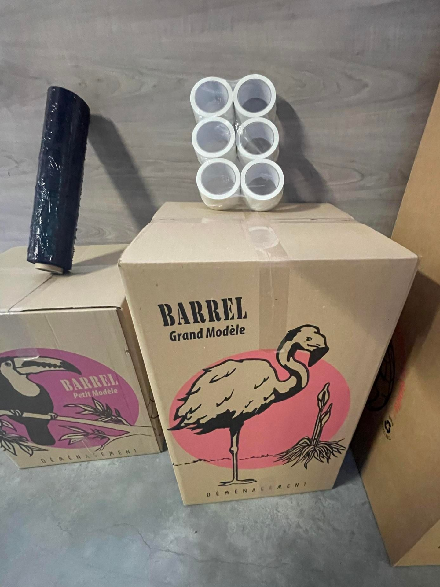 Des boîtes ornées de flamants roses, plusieurs scotches sur un carton et un film noir étirable.