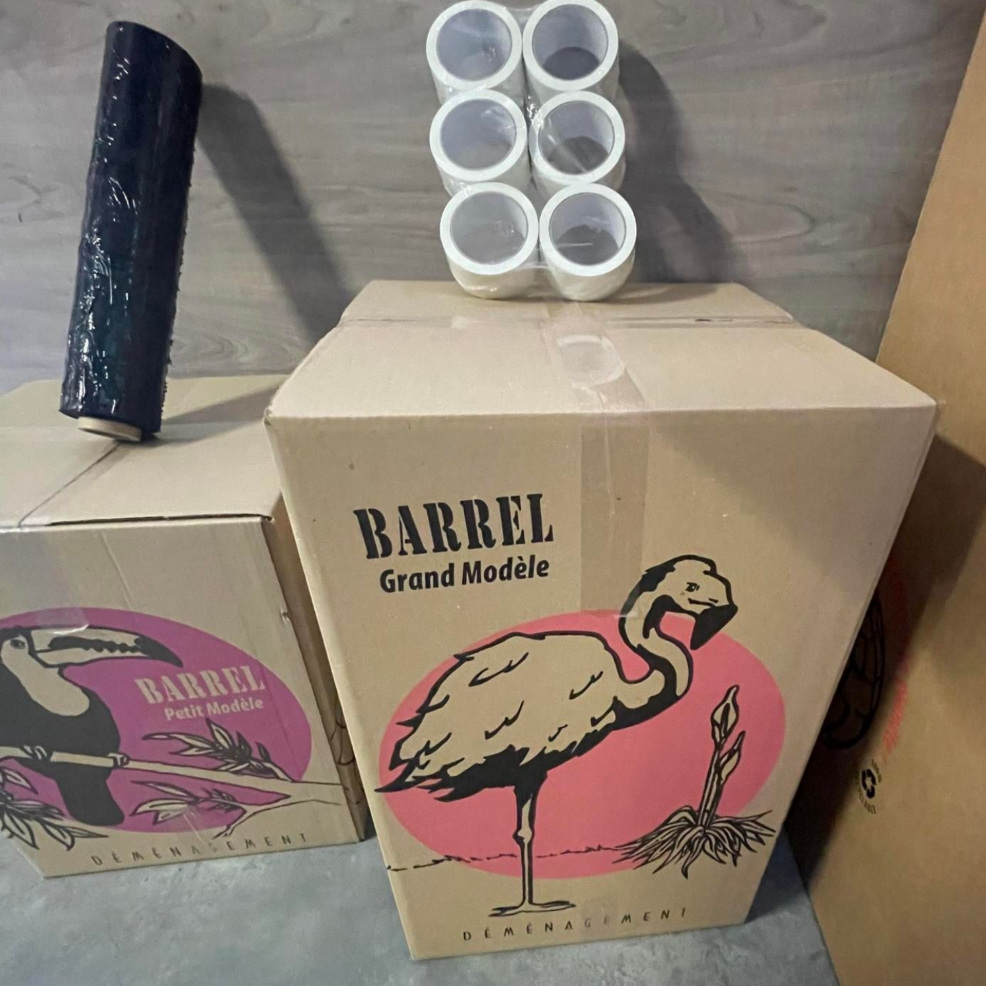 Des boîtes en carton décorées de flamants roses et de toucans, des fournitures d'emballage et de Scotch.