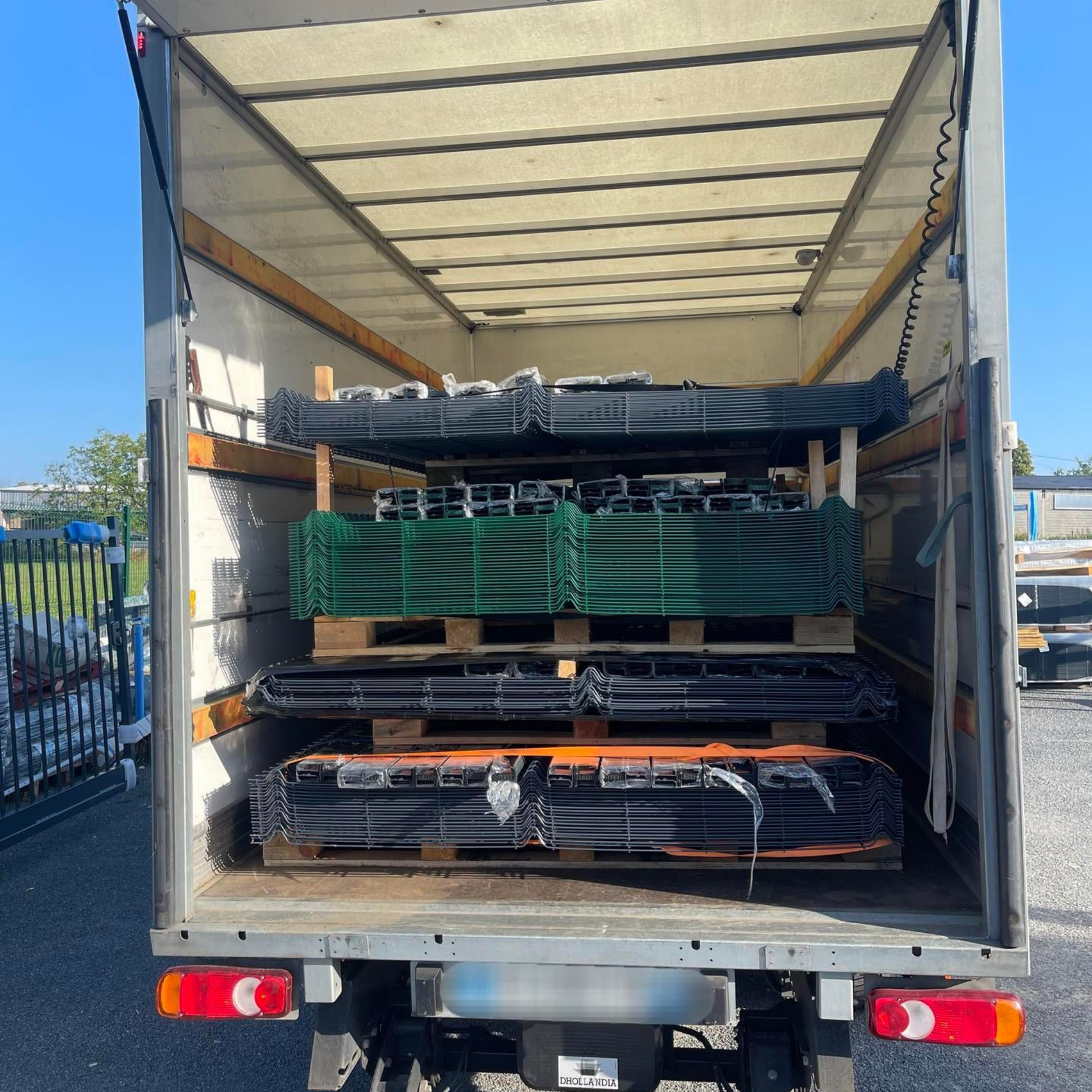 Plateau de camion ouvert chargé de panneaux de clôture métalliques sur palettes.