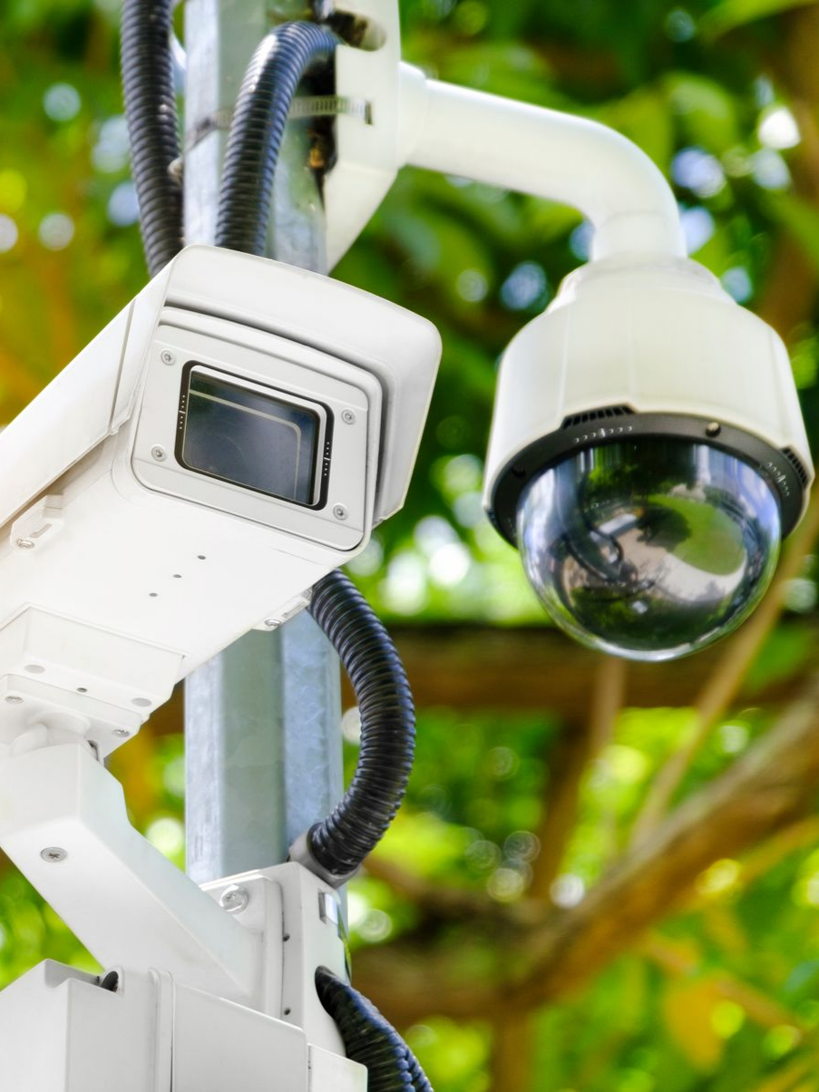 Deux caméras de sécurité blanches fixées sur un poteau, l'une rectangulaire, l'autre en forme de dôme.