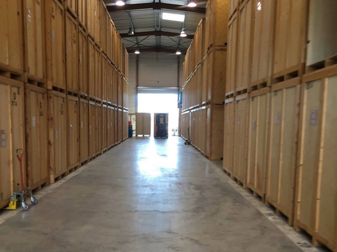 Long couloir d'un entrepôt, bordé d'étagères en bois empilées.