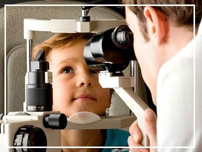 Un niño mira dentro de la máquina de examen ocular de un optometrista mientras un médico la ajusta.