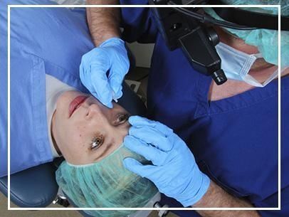 Odontólogo examinando los ojos de un paciente con guantes y una lámpara dental encendida.