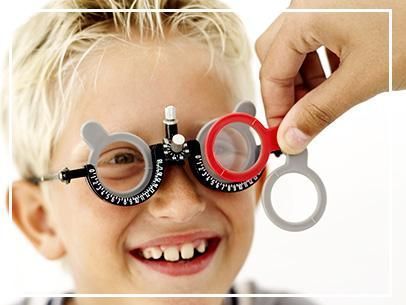 Un niño sonríe a través de unas gafas de fantasía mientras una mano sostiene una lente roja y blanca.
