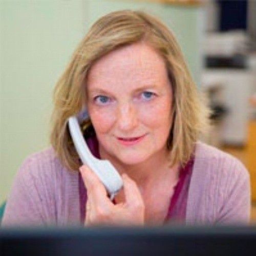 Mujer sosteniendo un receptor de teléfono, mirando hacia la cámara, entorno interior.