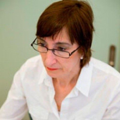 Mujer con gafas, mirando hacia abajo, con camisa blanca, en el interior.