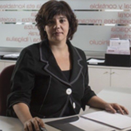 Mujer con chaqueta negra en un escritorio, mirando a la cámara.