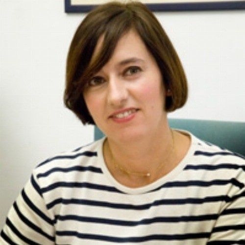Mujer de pelo corto y oscuro, vestida con una camisa de rayas, sonríe a la cámara.