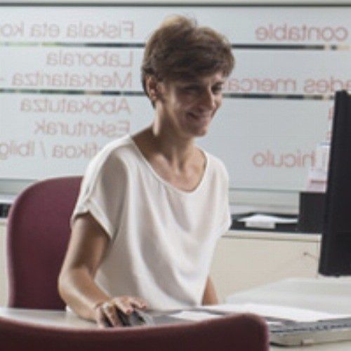 Mujer con top blanco, sentada en un escritorio, usando una computadora; fondo con texto.