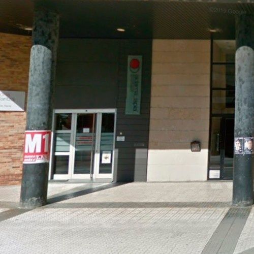 Entrada a un edificio con dos grandes pilares de soporte, puerta de vidrio y señalización.