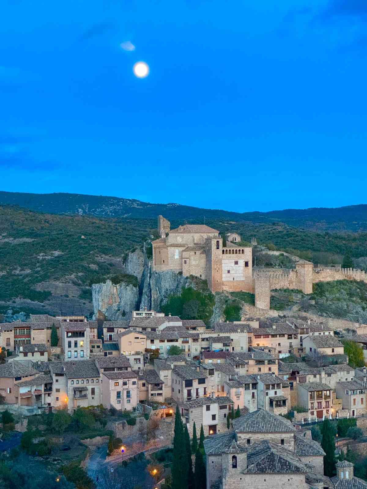 Un castillo medieval encaramado en un acantilado rocoso con vistas a un denso grupo de casas de piedra.