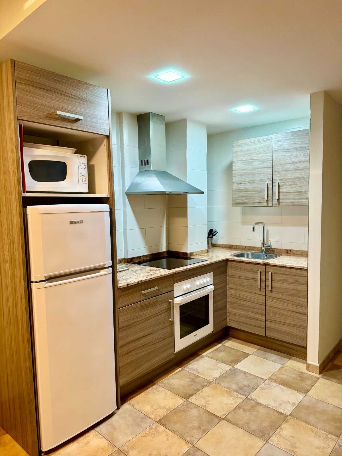 Una cocina compacta con armarios con acabado de madera, electrodomésticos blancos, campana extractora.