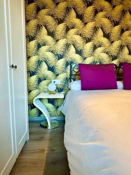 Un rincón de dormitorio con una mesita de noche curva blanca, un armario blanco y una cama con una almohada rosa brillante.