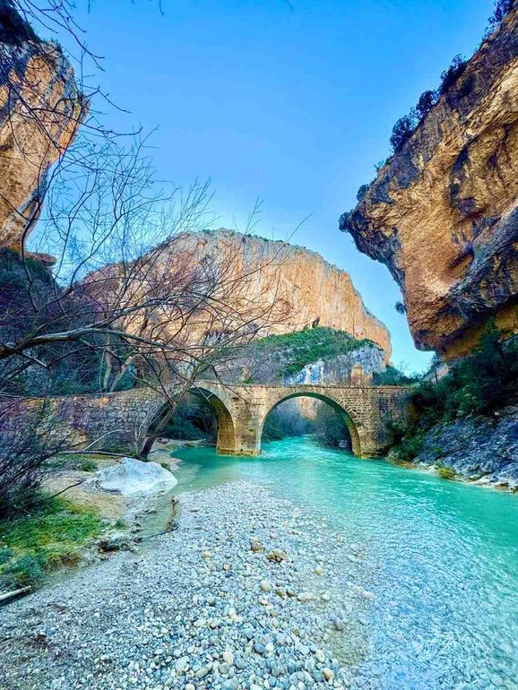 Un puente de arco de piedra atraviesa un río cristalino de color turquesa que fluye a través de un cañón.