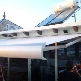 Toldo blanco sobre un patio con paneles solares en el tejado de un edificio.
