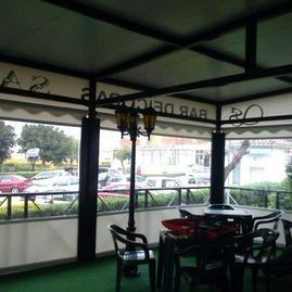 Terraza cubierta con mesas y sillas, con vistas a un aparcamiento y a la calle.