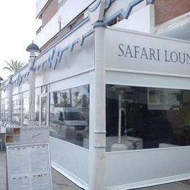 Exterior de la esquina del Safari Lounge con fachada blanca y grandes ventanales en una esquina de la calle.