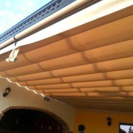 Primer plano de un toldo retráctil de color beige bajo el borde de un tejado sobre una puerta de patio.
