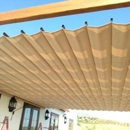 Toldo retráctil beige sobre un patio junto a una casa, con cielo azul arriba.