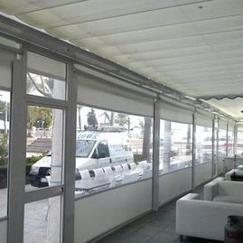 Patio cubierto con asientos blancos y paneles cortavientos de vidrio con vista a los autos estacionados.