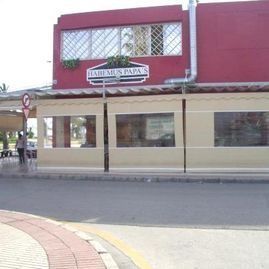 Vista de la calle de una tienda con fachada roja y crema y un letrero, vista al otro lado de una calle tranquila.