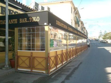 Cafetería de esquina con toldo amarillo y patio con paneles de madera en una calle tranquila.