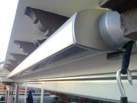 Primer plano de un toldo retráctil con tela blanca y estructura metálica bajo un alero.