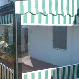 Pequeño patio o porche con toldos de rayas verdes y blancas y paredes blancas, visto desde el exterior.