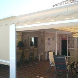 Patio cubierto con suelo de baldosas, sillas de exterior y mesa junto a una casa con paredes de ladrillo.