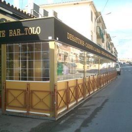 Bar de esquina con toldo negro y detalles amarillos en una calle soleada de la ciudad.