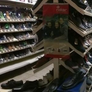 Gang in einem Schuhgeschäft mit Reihen von Schuhen in Regalen und einem zentralen Ausstellungsständer mit einem Werbeschild.