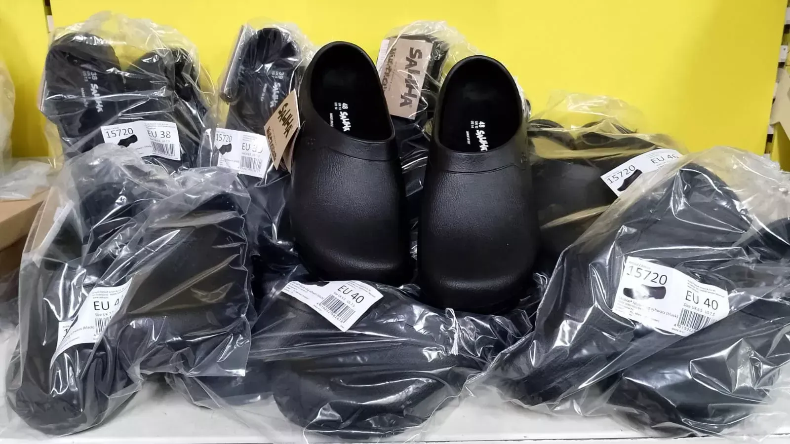 Schwarze, in Plastik verpackte Schuhe, gestapelt vor einem leuchtend gelben Hintergrund