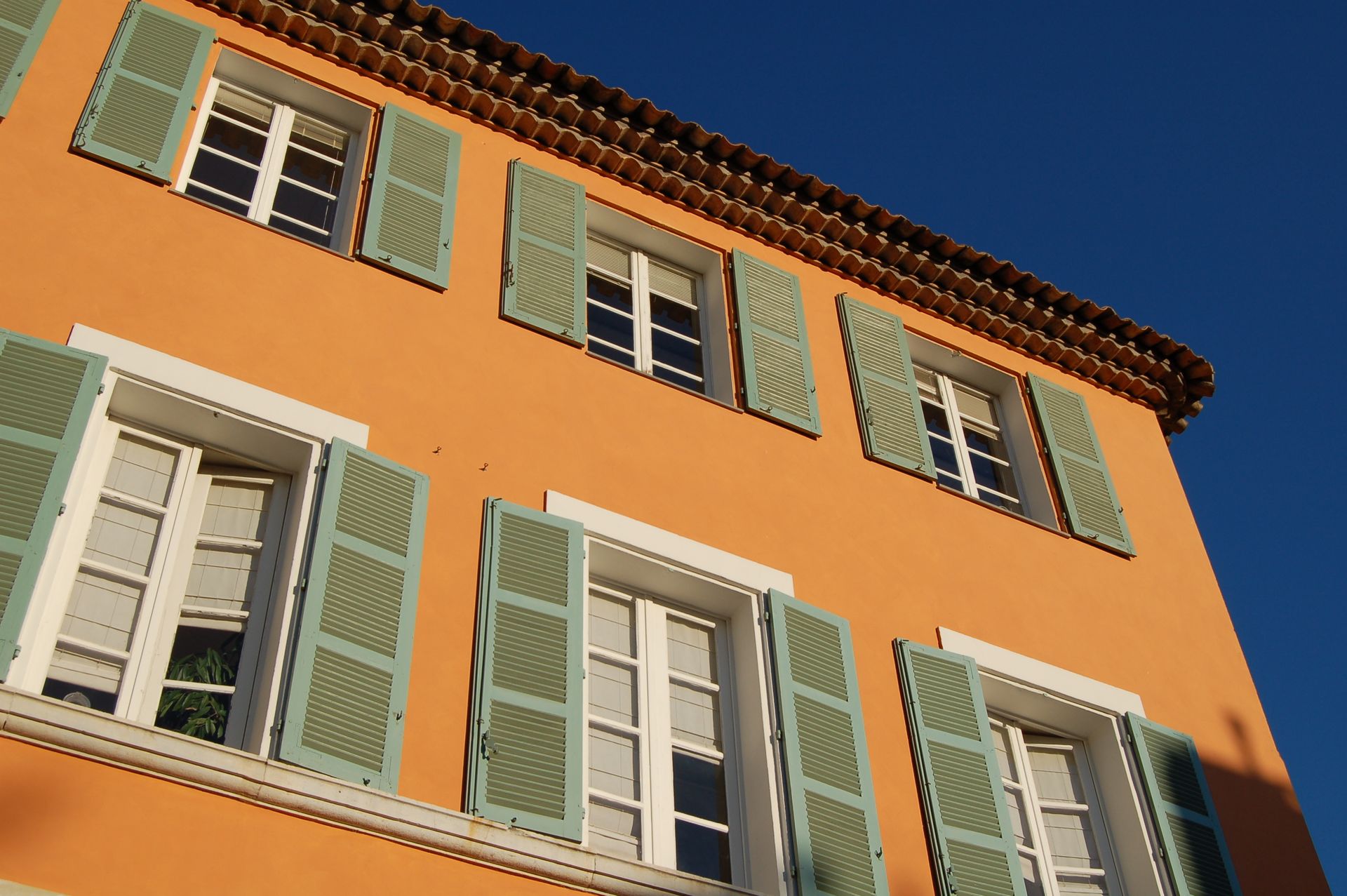 Façade d'une maison de couleur orange avec des volets verts
