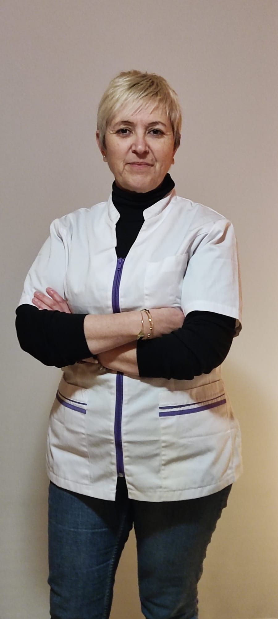 Una mujer con un abrigo blanco y un cuello alto negro está de pie con los brazos cruzados.
