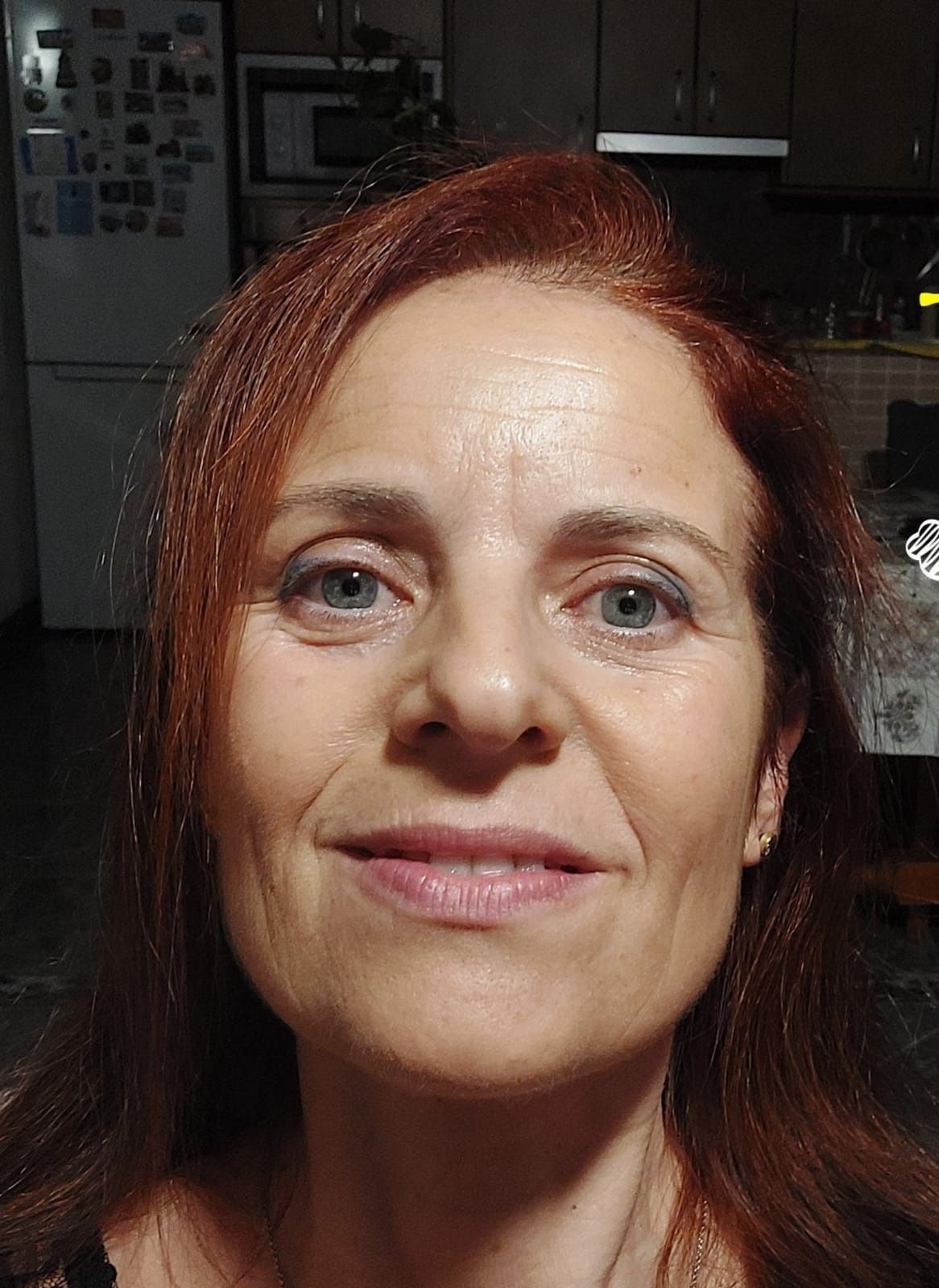 Una mujer con cabello rojo y ojos azules está sonriendo en una cocina.