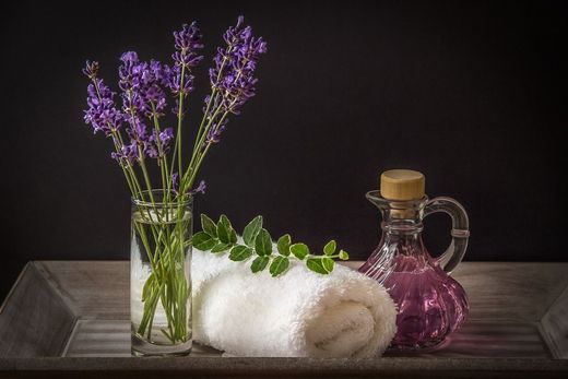 Una toalla, un jarrón con flores y una botella de aceite esencial están sobre una bandeja de madera.